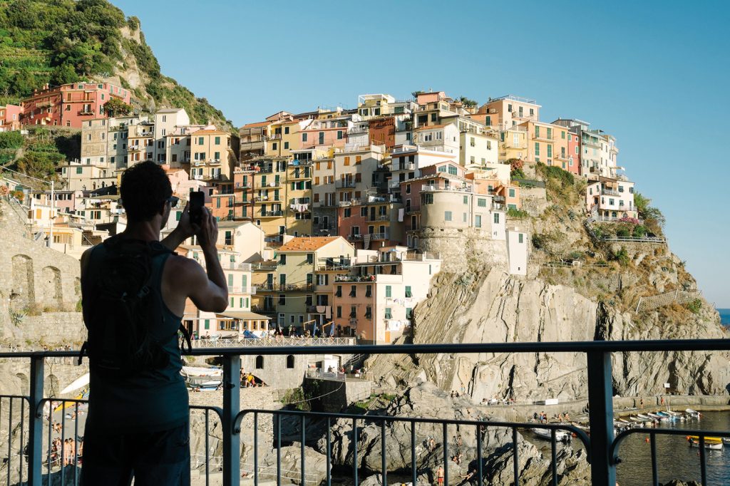 64693926 - manarola, italy - august 24, 2016: silhouette of a tourist photographing with smartphone the view of manarola, cinque terre liguria.
